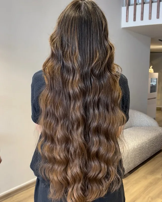 Longs cheveux châtains ondulés après un brushing, vus de dos dans le salon