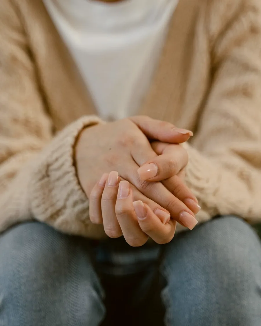Mains aux ongles soignés posées l'une sur l'autre, dans un pull crème