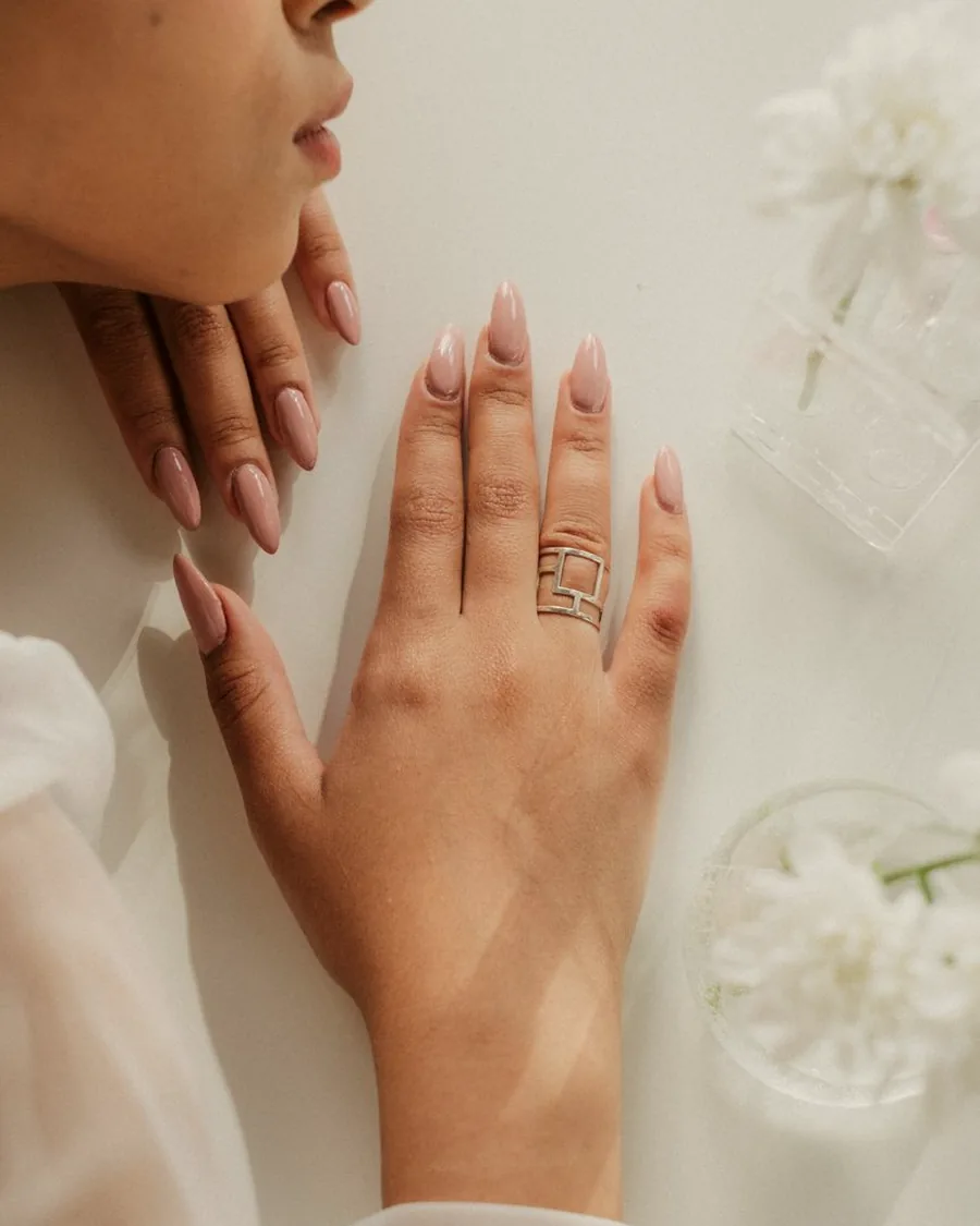 Main aux ongles nude en amande posée sur une table claire